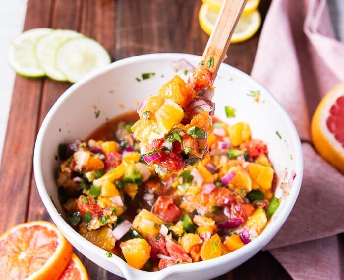 A spoon holing some citrus salsa close up showing the details and textures and how juicy the salsa