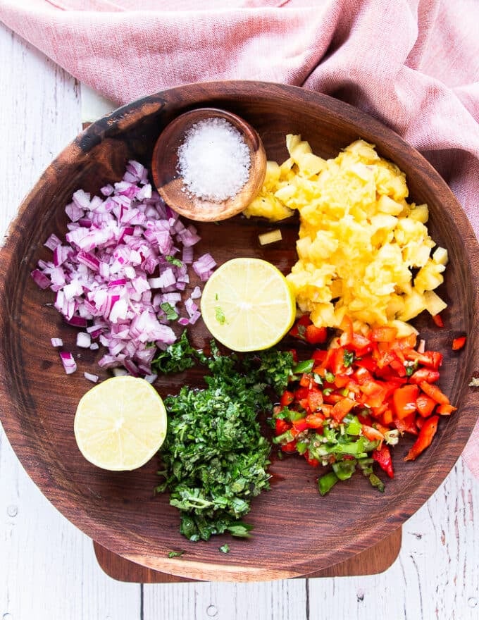 The ingredients for pineapple salsa are finely diced in a large wooden bowl 