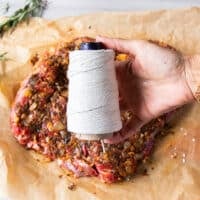 A hand holding a kitchen twine to begin tying up the boneless leg of lamb for roasting