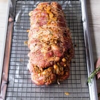 The tied up boneless leg of lamb is placed over a wire rack over a baking sheet and ready to marinate or begin roasting