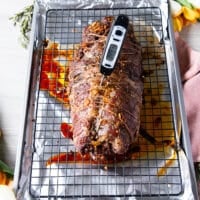 The slow roasting of the boneless leg of lamb is completed the first half at low temperature and a meat thermometer is showing the perfect temperature