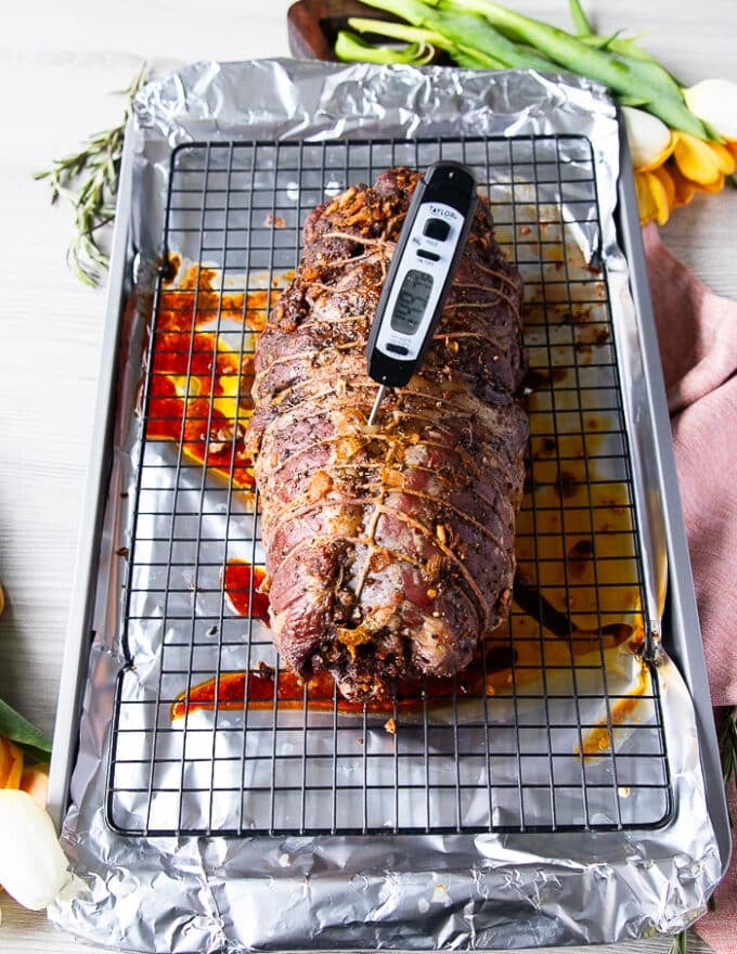 The slow roasting of the boneless leg of lamb is completed the first half at low temperature and a meat thermometer is showing the perfect temperature 