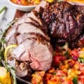 close up of roasted boneless leg of lamb on a bed of citrus salsa surrounded by fresh rosemary