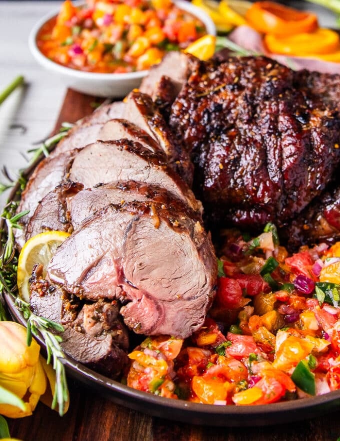 close up of roasted boneless leg of lamb on a bed of citrus salsa surrounded by fresh rosemary 