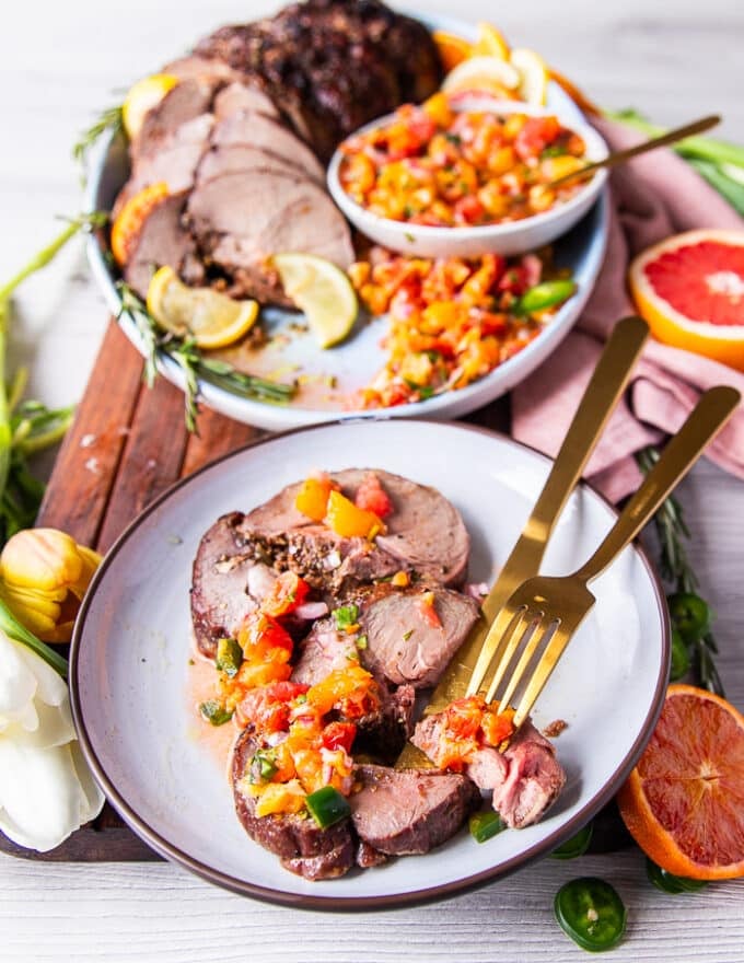 Two thick slices of boneless leg of lamb roasted and served on a small plate with some salad and a fork and knife cutting through