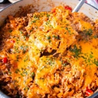 A spoon taking out a portion from the stuffed peppers casserole to serve on a plate showing the stretchy cheese