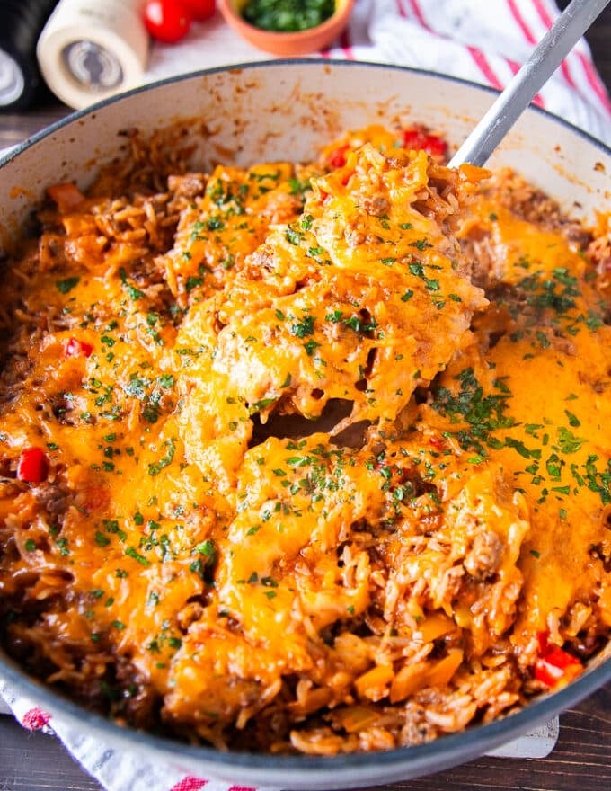A spoon taking out a portion from the stuffed peppers casserole to serve on a plate showing the stretchy cheese 