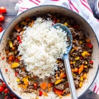 The basmati rice is added to the skillet of peppers and meat
