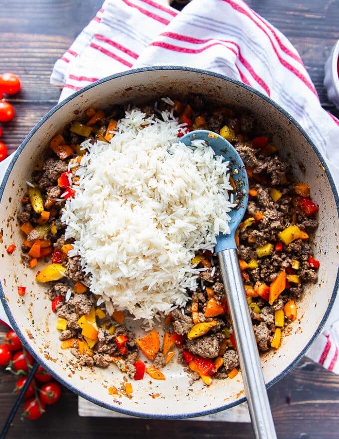 The basmati rice is added to the skillet of peppers and meat