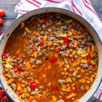 The tomatoes and stock is added to the skillet to cook the stuffed peppers casserole.