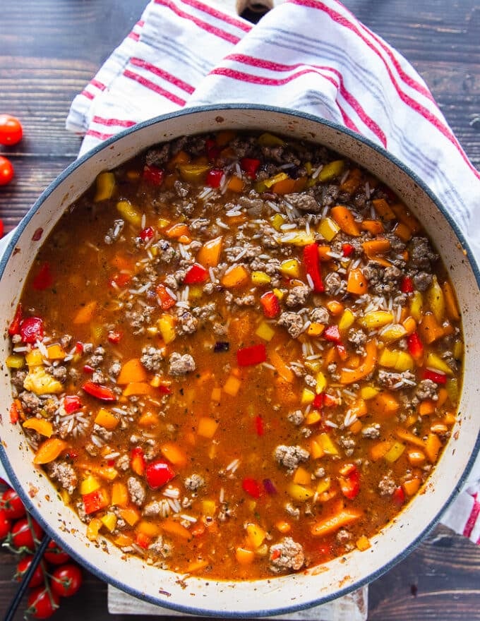 The tomatoes and stock is added to the skillet to cook the stuffed peppers casserole.