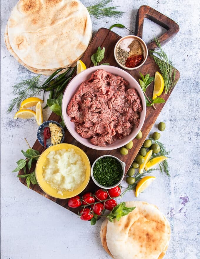 Arayes Ingredients: a bowl of minced lamb or beef or combo, bowl of minced onions, a bowl of minced herbs, a bowl of minced garlic, a bowl of tomato paste, a plate of seasoning spices, a variety of pita breads 