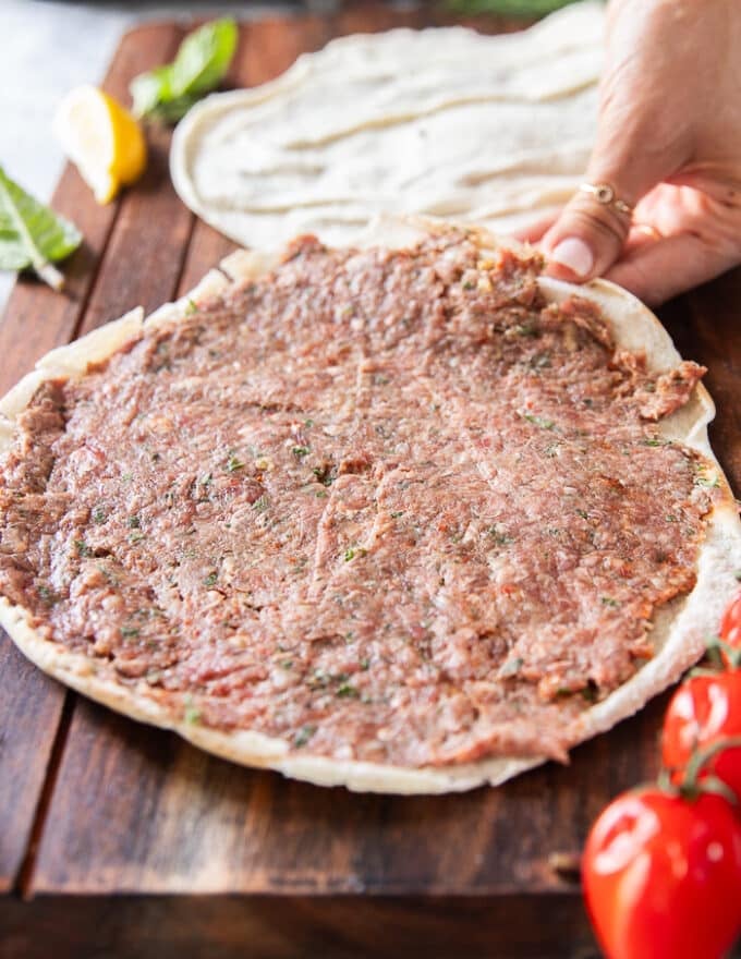 A thin layer of the meat mixture is spread over half of the pita bread