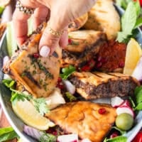 A hand holding a piece of cooked arayes and dipping it into the hummus