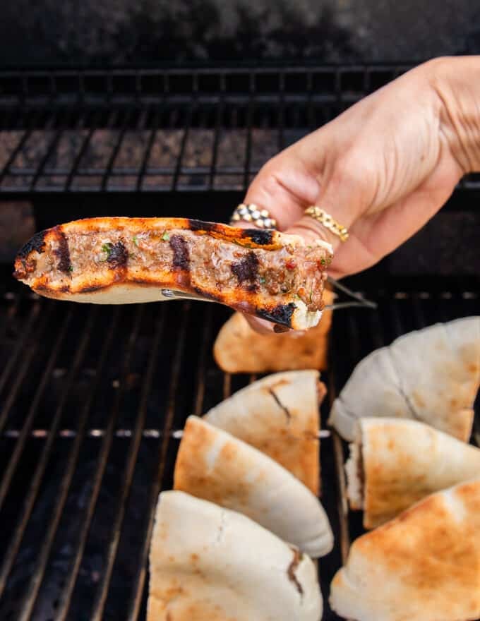 Arayes cooked on the grill and a hand holding the arayes showing the grill mark before flipping and grilling 