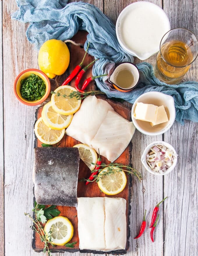 ingredients for the black cod recipe including black cod fillets, salt and pepper, some butter in a bowl, some cream in a cup, diced shallots in a bowl, lemon juice in a cup, some fresh herbs 