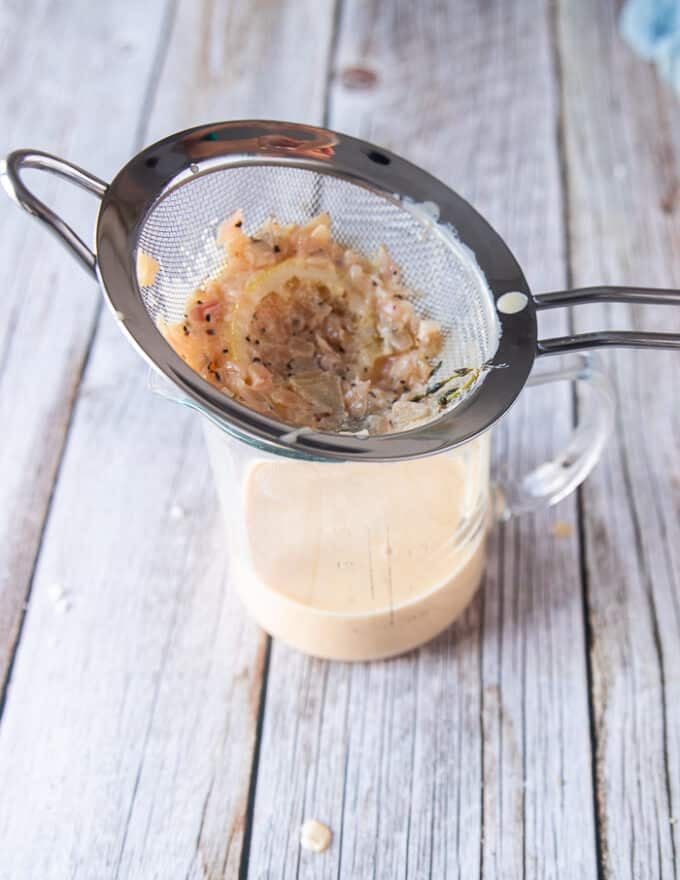 The creamy lemon sauce for black cod recipe is ready and passed through a sieve to strain in a cup 