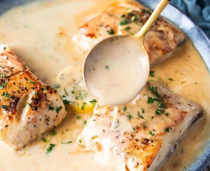 A spoon pouring some cream butter sauce over the black cod recipe to flavor it