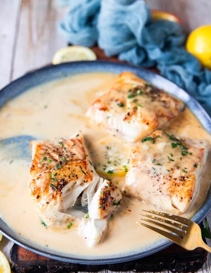 Full plate of black cod recipe in sauce and one of them broken with a fork to show the texture. 