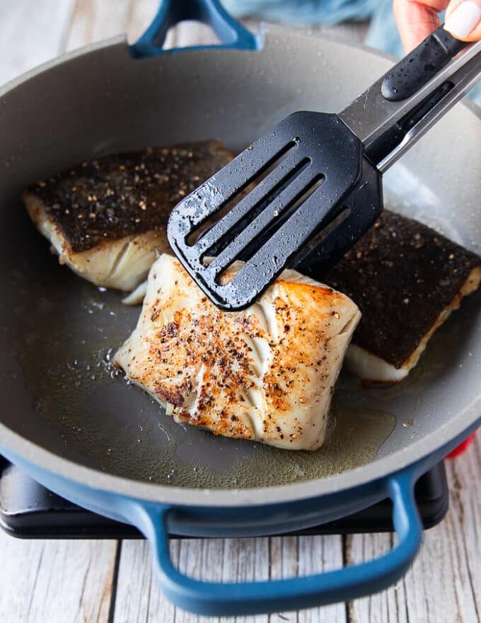 Flipped and golden black cod fish in the skillet ready to be removed