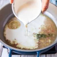 A hand pouring the cream over the shite wine sauce to finish the beurre blanc or creamy lemon sauce for black cod recipe