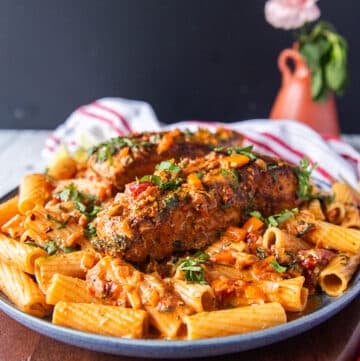 A plate of cajun pasta with plenty of cajun sauce and topped with a cajun halibut for extra protein surrounded by a vase with flowers