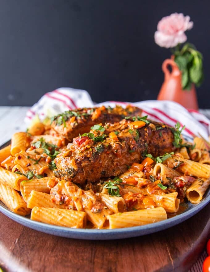 A plate of cajun pasta with plenty of cajun sauce and topped with a cajun halibut for extra protein surrounded by a vase with flowers 