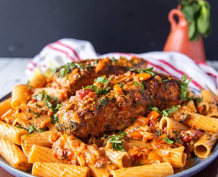 A plate of cajun pasta with plenty of cajun sauce and topped with a cajun halibut for extra protein surrounded by a vase with flowers