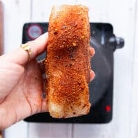 a hand holding cajun seasoned fish or chicken on both sides