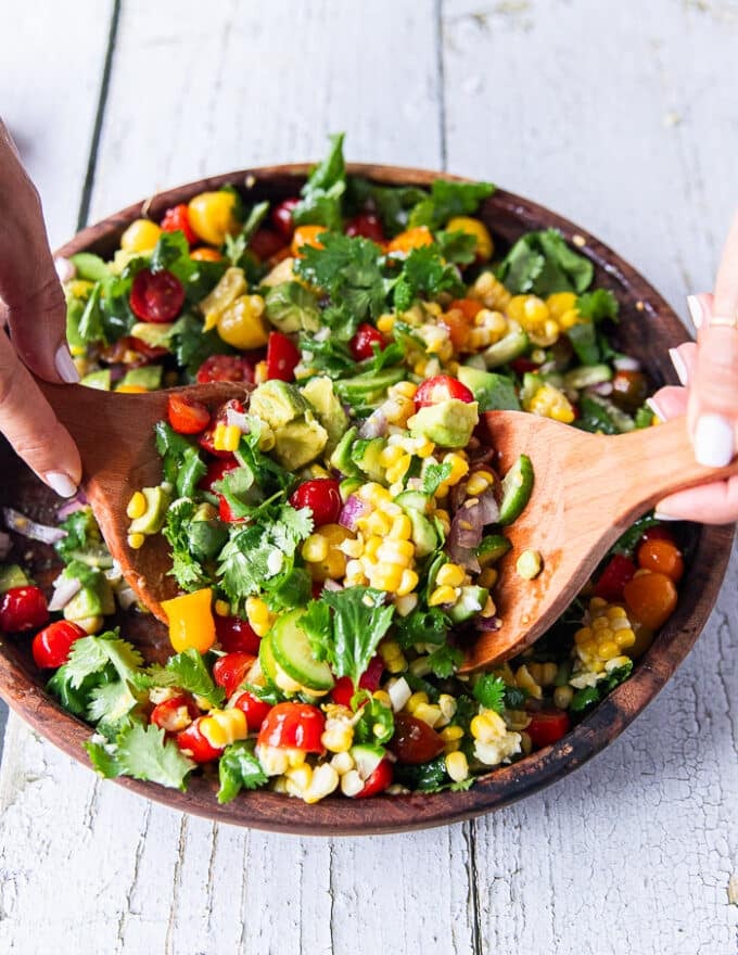 Corn and Tomato Salad in a large wooden bowl with two wooden spoons