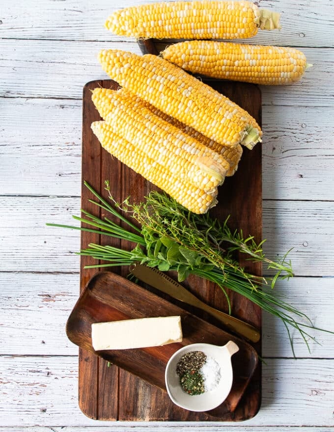 ingredients for how to boil corn on the cob. including fresh corn on the cob, some butter, some fresh herbs, some spice blend like salt and pepper