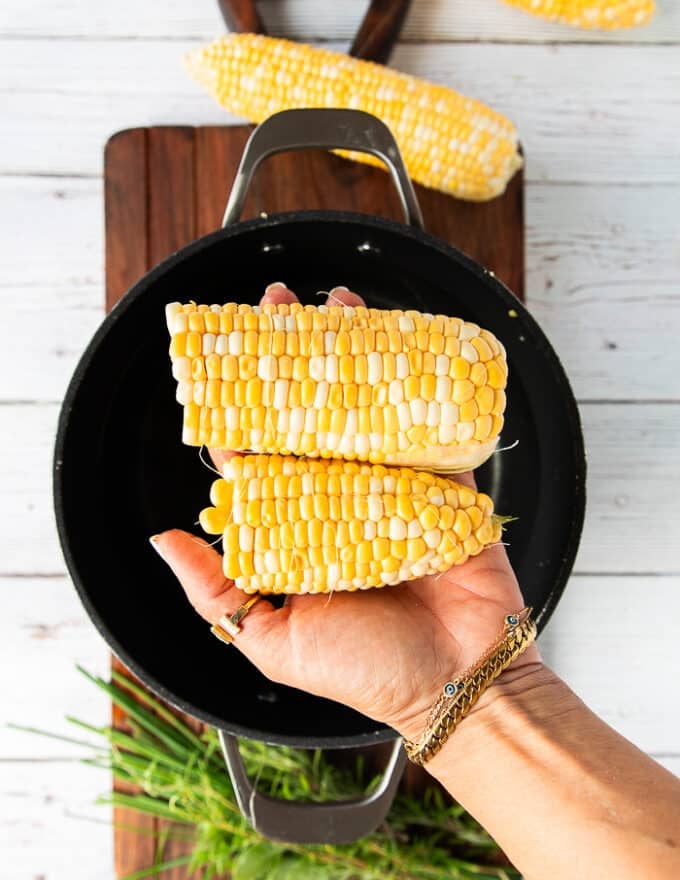 a hand holding a cleaned corn on the cub with rusks and hair removed and optionally cutting it in half
