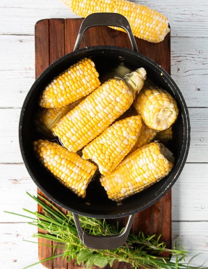 the corn is added to a pot of water and placed over the stove to begin boiling and cooking