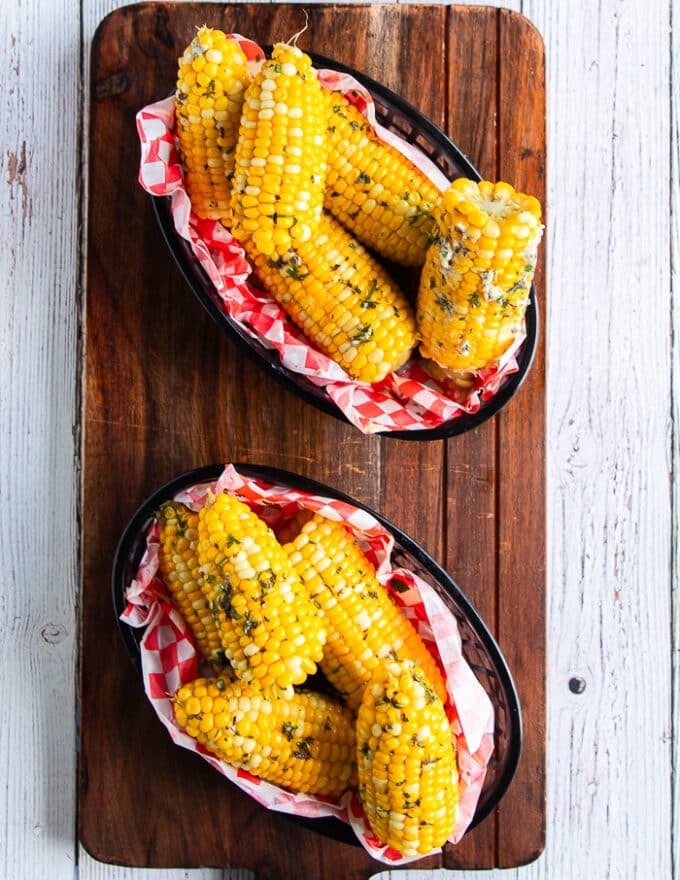 two plates of fully cooked and boiled corn on the cob served with herb butter