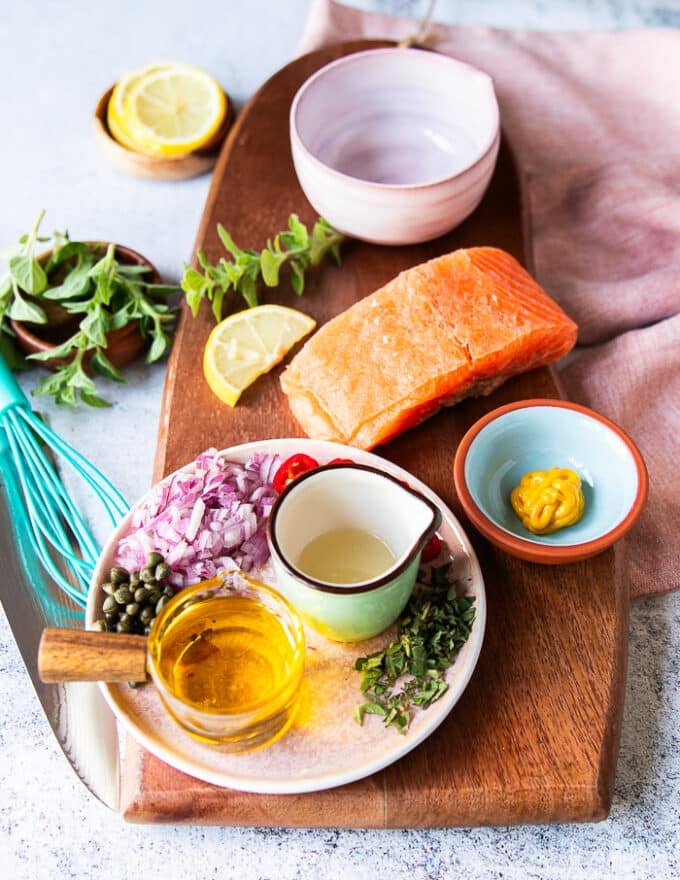Ingredients for salmon carpaccio including sushi grade salmon, mustard in a bowl, olive oil in a cup, some capers in a bowl, shallots in a bowl some herbs minced, some lemon juice in a bowl , salt and pepper 