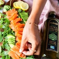 a hand arranging the thinly sliced salmon over a bed of arugula
