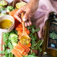 A hand holding a spoonful of the vinaigrette and dressing the salmon slices with it to marinate and season the salmon carpaccio