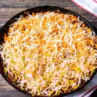 Cheese is sprinkled over the taco spaghetti in the cast iron and it's now ready to bake