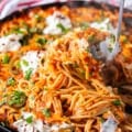 A pasta spoon scooping up some taco spaghetti from the pan showing the stretch of cheese with spaghetti with the taco meat and sauce