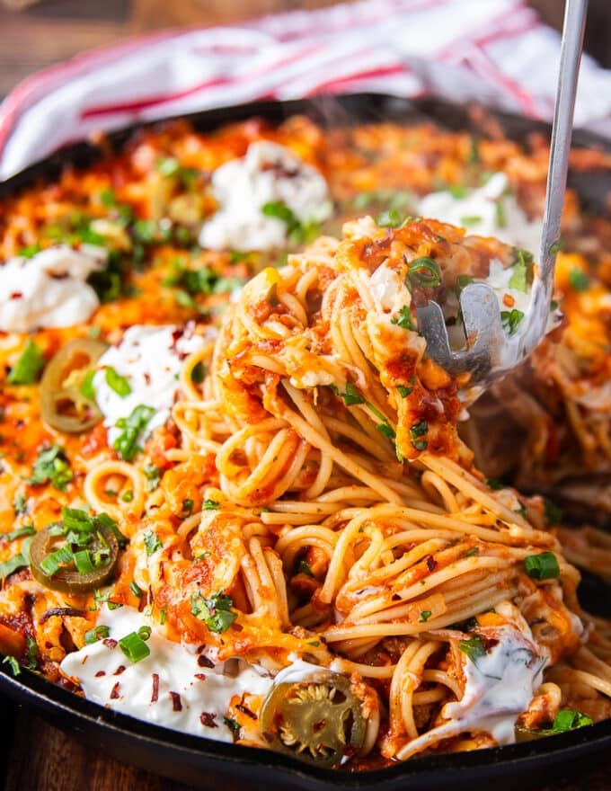 A pasta spoon scooping up some taco spaghetti from the pan showing the stretch of cheese with spaghetti with the taco meat and sauce
