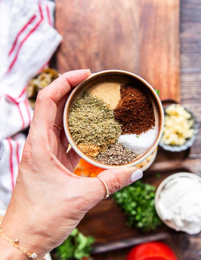 A hand holding a plate of taco seasoning ingredients to show you can make it at home 
