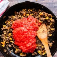 crushed tomatoes and corn are added into the ground beef skillet and the sauce is simmering