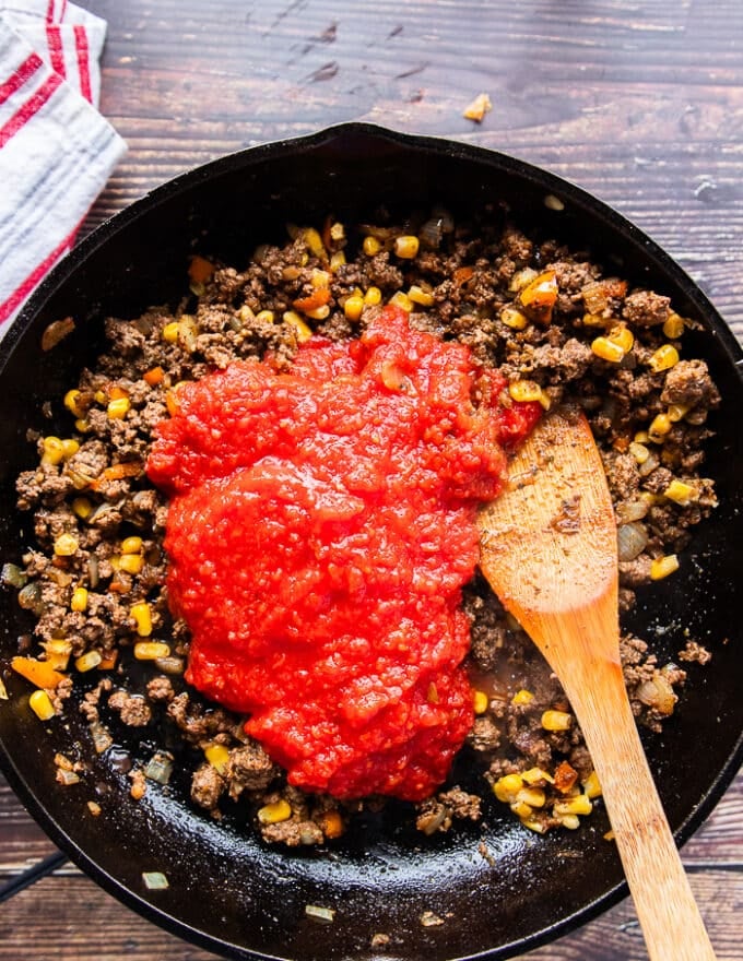 crushed tomatoes and corn are added into the ground beef skillet and the sauce is simmering 