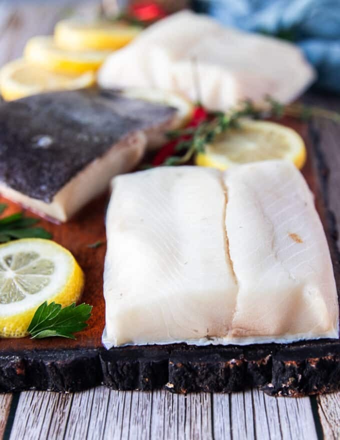 Raw black cod filets on a wooden board close up showing the texture and dark black skin 