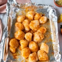 scallops tossed in seasoning and melted butter on a foil lined baking sheet