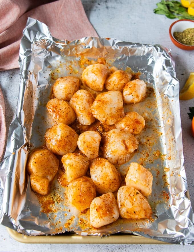 scallops tossed in seasoning and melted butter on a foil lined baking sheet