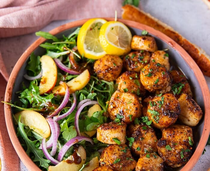 A plate of broiled scallops served with lemon slices and a side of salads