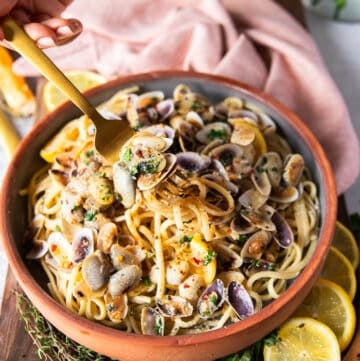 A fork stretching the clam pasta showing the details of the spaghetti and the cooked clams in the simple clam sauce with some lemon slices and chilli flakes