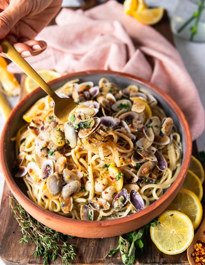 Un tenedor que estira la pasta de almeja que muestra los detalles de los espagueti y las almejas cocidas en la salsa de almeja simple con algunas rebanadas de limón y copos de chile