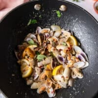 fully cooked clams in a skillet with lemon slices, garlic and chilli flakes, all clams have opened and cooked and ready to make clam pasta